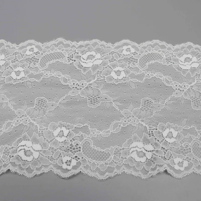 Une section à plat de large dentelle blanche à motifs floraux montrant des bords festonnés assortis.