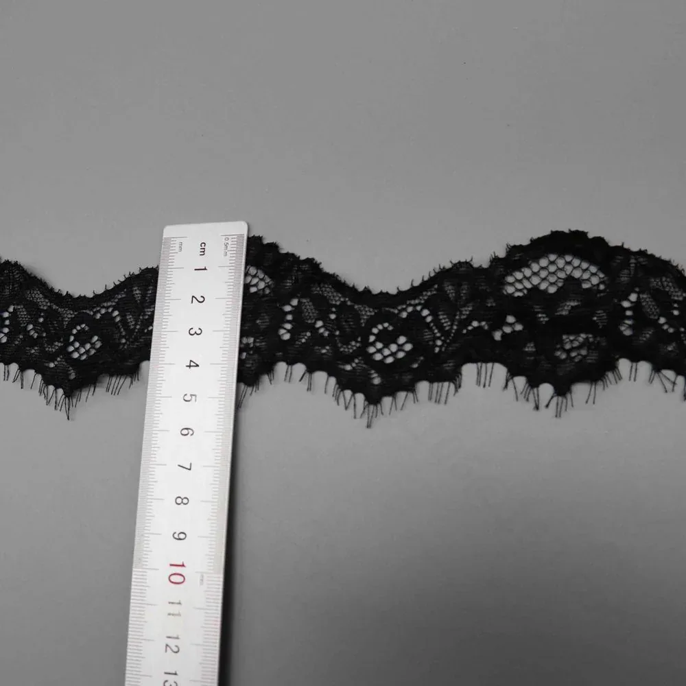 A ruler placed across black floral eyelash lace trim. A ruler placed across black floral eyelash lace trim.