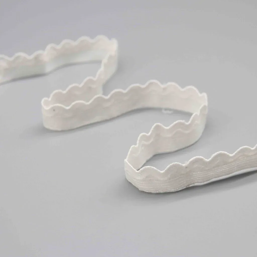 Galon blanc festonné disposé en ondulations souples sur une surface grise.