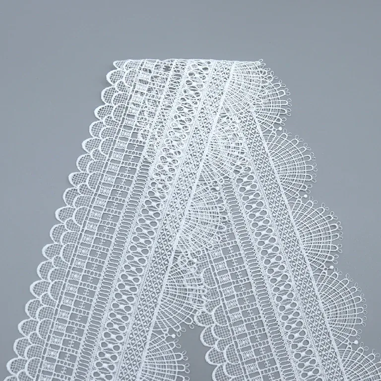 White geometric lace trim folded on a gray surface, showing fan-shaped edges. White geometric lace trim folded on a gray surface, showing fan-shaped edges.