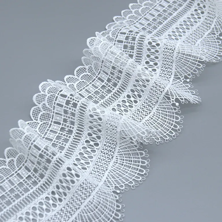 White fan-edged lace trim arranged in loose waves on a gray surface. White fan-edged lace trim arranged in loose waves on a gray surface.