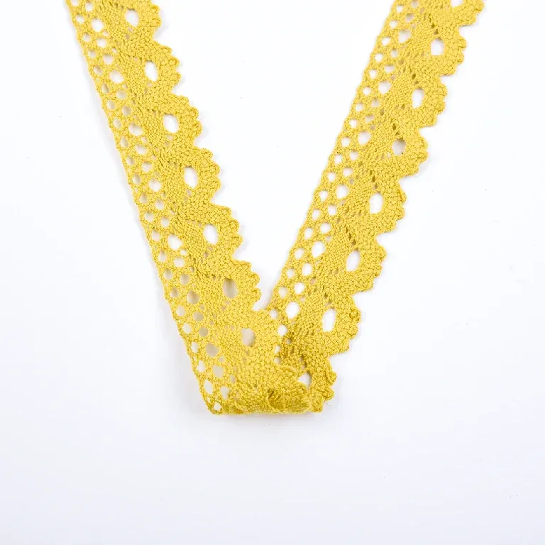 Galon de dentelle jaune à coquilles en éventail plié en V sur une surface blanche.