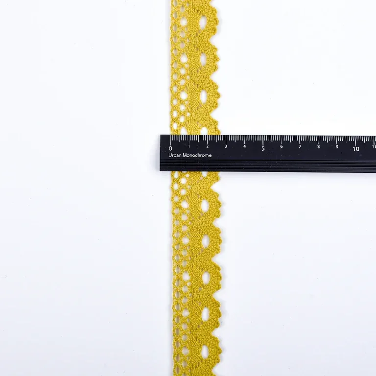 Une règle noire placée en travers d’un galon de dentelle jaune à coquilles en éventail sur une surface blanche.