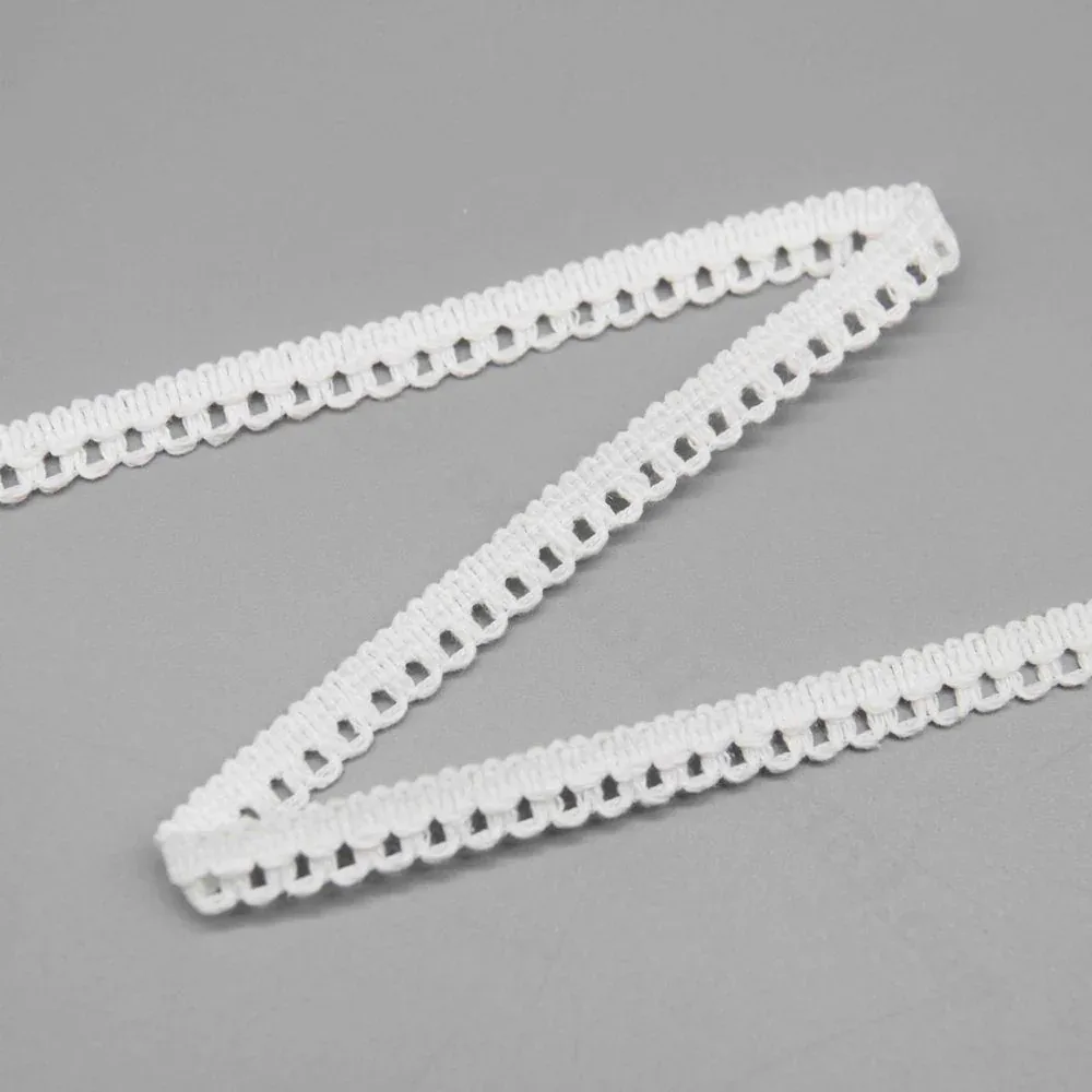 Tira de encaje blanco con bucles de picot dispuesta en zigzag sobre una superficie gris.