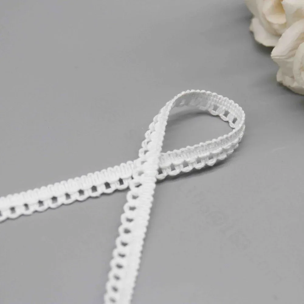 Tira de encaje blanco con bucles de picot dispuesta formando un aro junto a flores de tonos claros.