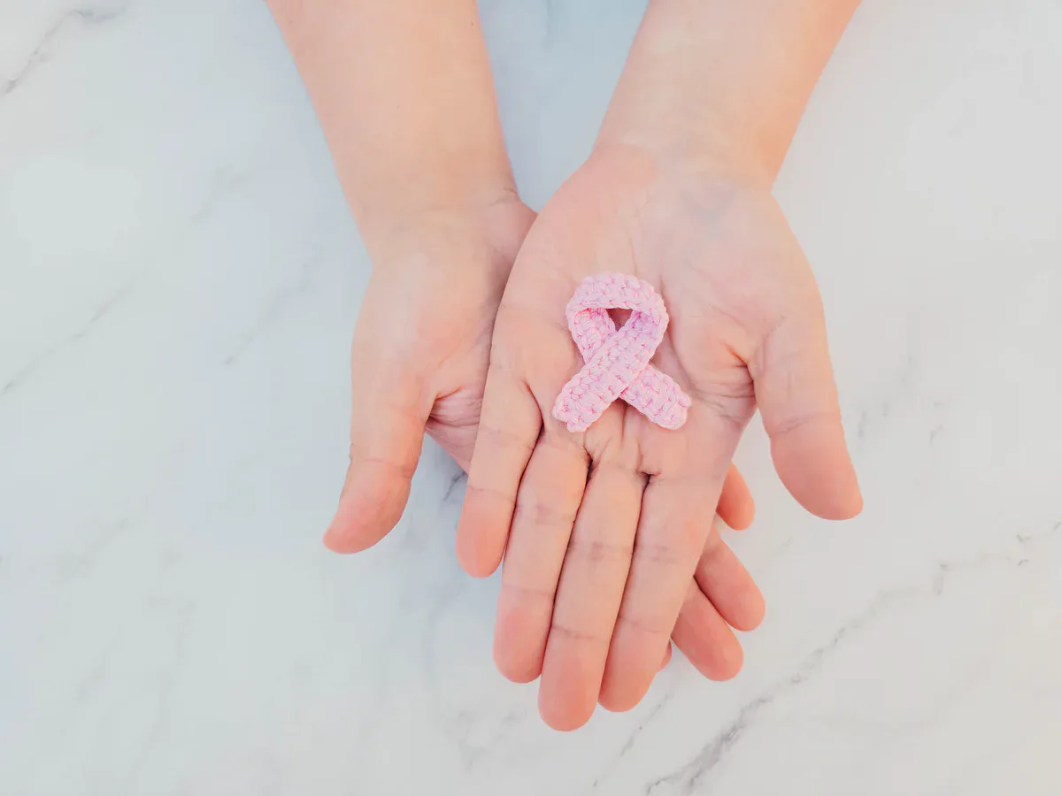 Un lazo rosa tejido a ganchillo descansa sobre unas manos abiertas Un lazo rosa tejido a ganchillo descansa sobre unas manos abiertas