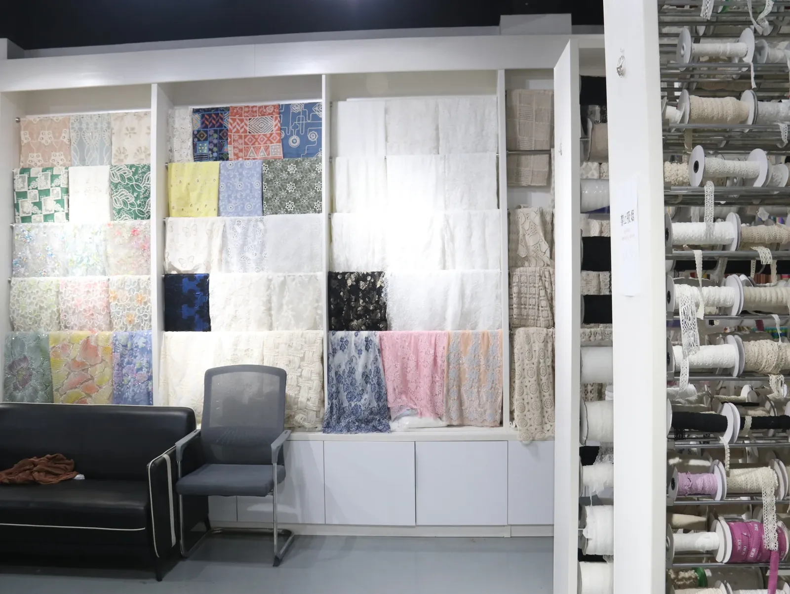Échantillons de tissus et de galons de dentelle présentés à côté de rouleaux d’échantillons dans les locaux de YiTuo Lace.