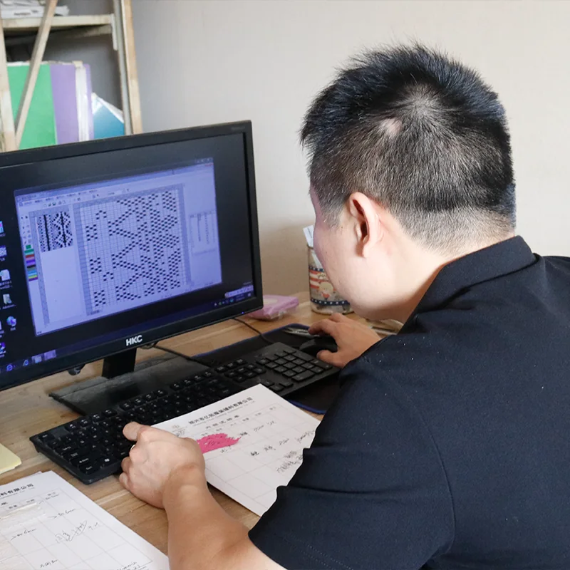 A team member working on a lace pattern at a computer with a pink sample on the desk.