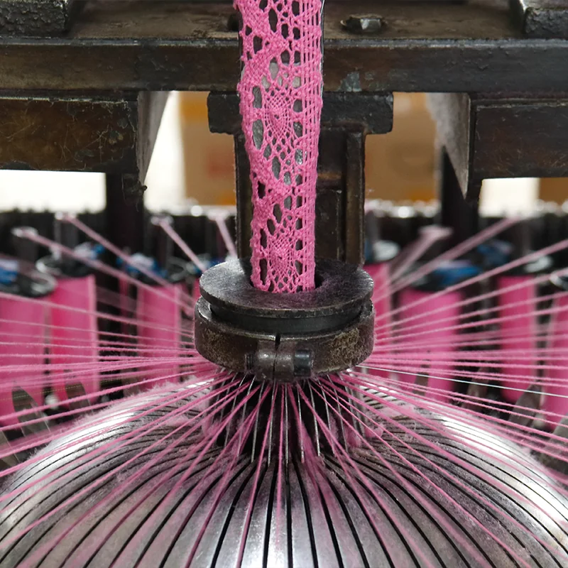 Bright pink threads feeding a machine as a strip of pink lace takes shape.