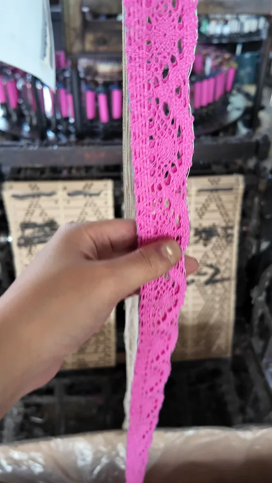 A hand holding bright pink lace to show its floral pattern, openwork and edge.