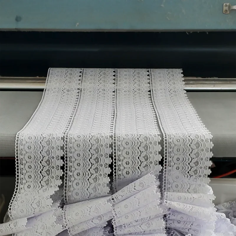 White openwork lace strips with repeating motifs at finishing equipment.