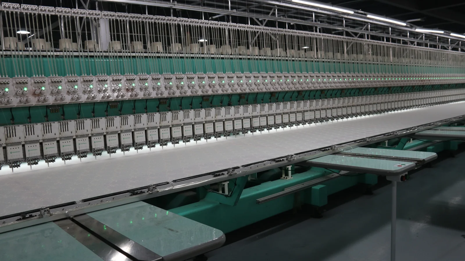 Ligne de broderie industrielle Longue rangée d’équipements de broderie verts avec guides-fils et tables de travail