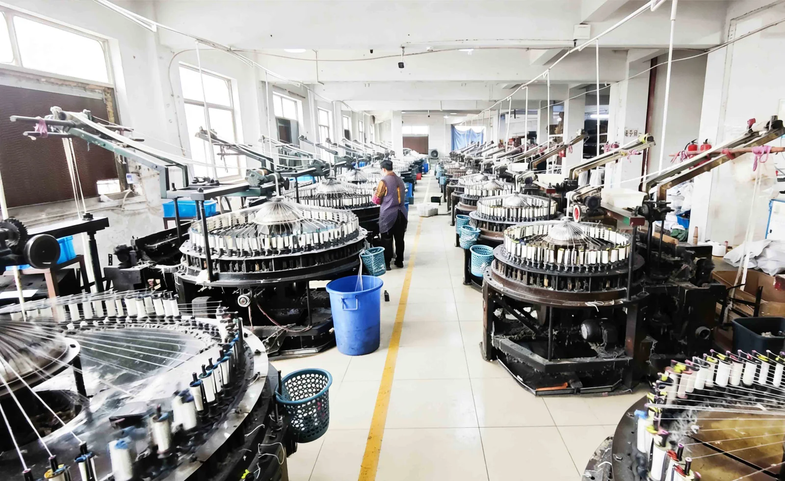 Allée de l’atelier de tricotage Machines à tricoter circulaires et récipients bleus le long d’une allée lumineuse de l’atelier