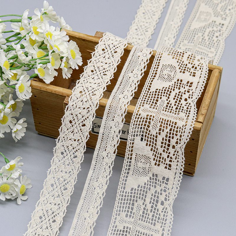 Beige cotton thread lace trims featuring detailed crochet patterns and vintage motifs displayed on a wooden box next to white daisies.