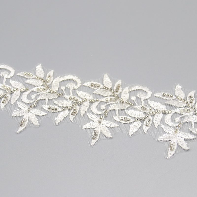 Elegant white lace trim showcasing detailed leaf embroidery and sparkling bead decorations, suitable for bridal wear.