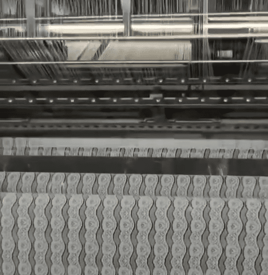 Row of multi‑needle computerized embroidery machines producing delicate lace trims for apparel, lingerie, and home textiles inside a modern factory.