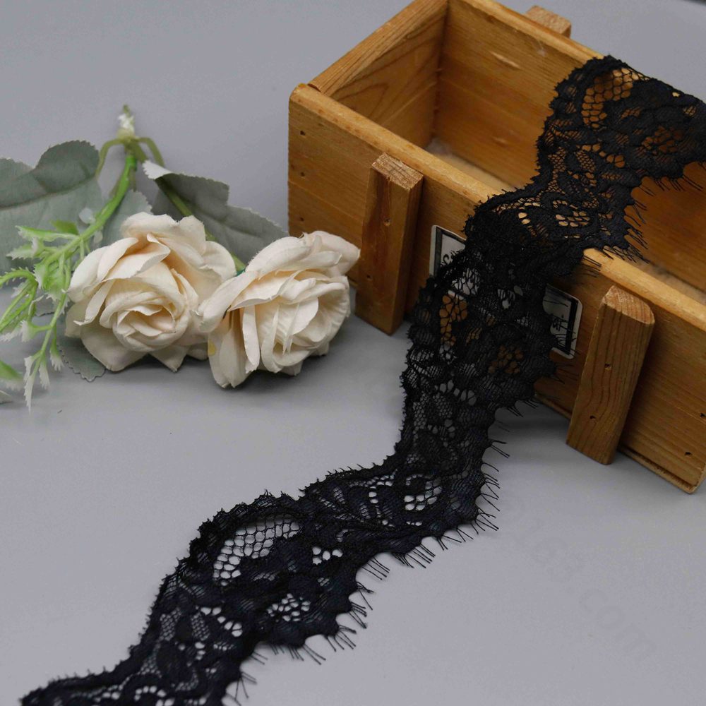 High-resolution image of fancy French lace trim ribbon in classic black and white, showcasing layered floral motifs with intertwined flowers and leaves on a breathable mesh; soft stretch and irregular scalloped edges with fine eyelash strands add dynamic elegance, perfect for ladies' necklines and intimate lingerie.