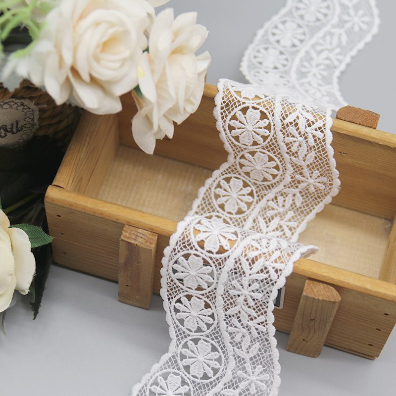 Detailed view of designer French customizable lace trim in crisp white, highlighting refined mesh embroidery with prominent 3D circular geometric patterns and petal-like rays in multi-layered precision; flowing micro-wave contours add sophistication to clothing accessories and bespoke designs.