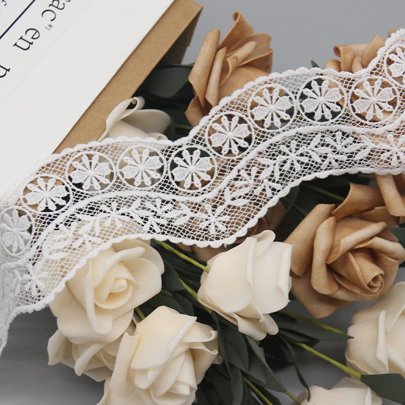 Refined image of customizable French lace trim in pure white, with intricate mesh embroidery highlighting 3D geometric circular designs filled with layered radiating petals for depth and elegance; micro-wave edges with fluid lines ideal for designer garment accessories and personalized style.