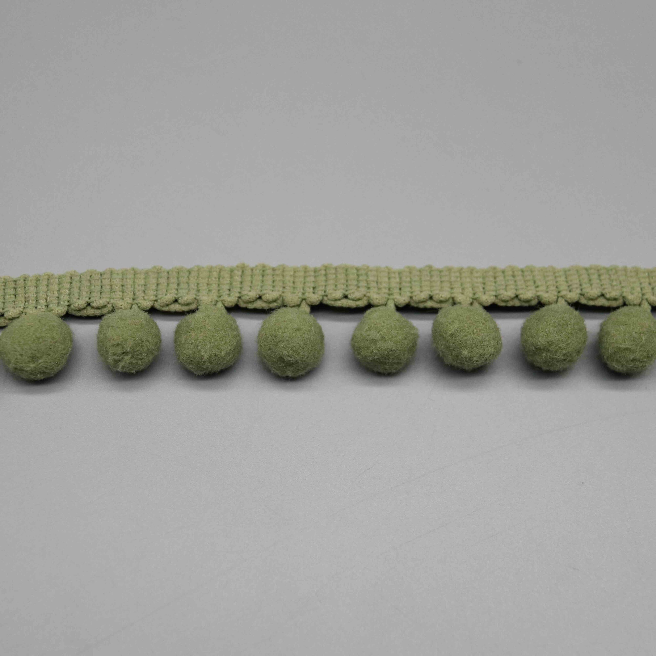 Macro close-up of the plush fuzzy pompom texture and olive green fiber surface.