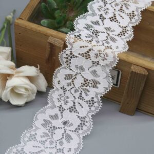 Studio photo of a 5cm wide white stretch galloon lace, featuring a symmetrical floral scroll pattern and double scalloped edges