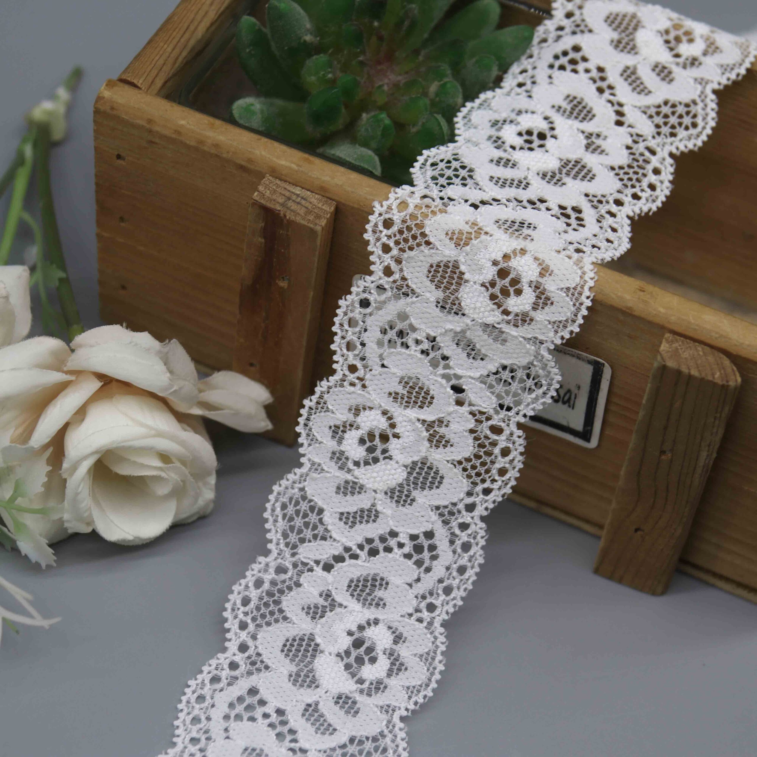 floral stretch lace trim with a scalloped edge, measured against a ruler on a gray background.