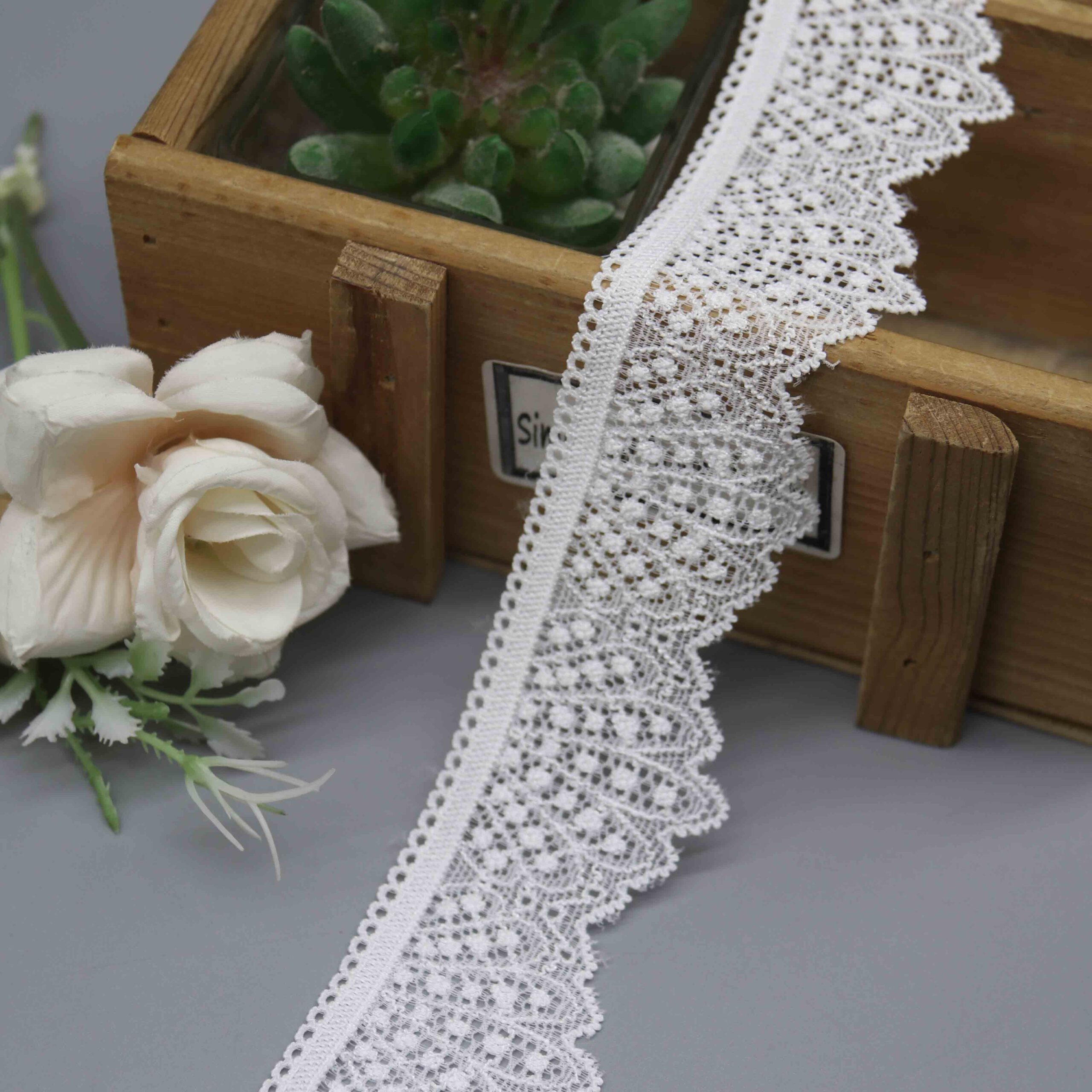 A studio photo of a 4.5cm wide white scalloped edge stretch lace, highlighting its asymmetrical design with a straight heading and a decorative fan-scallop edge.
