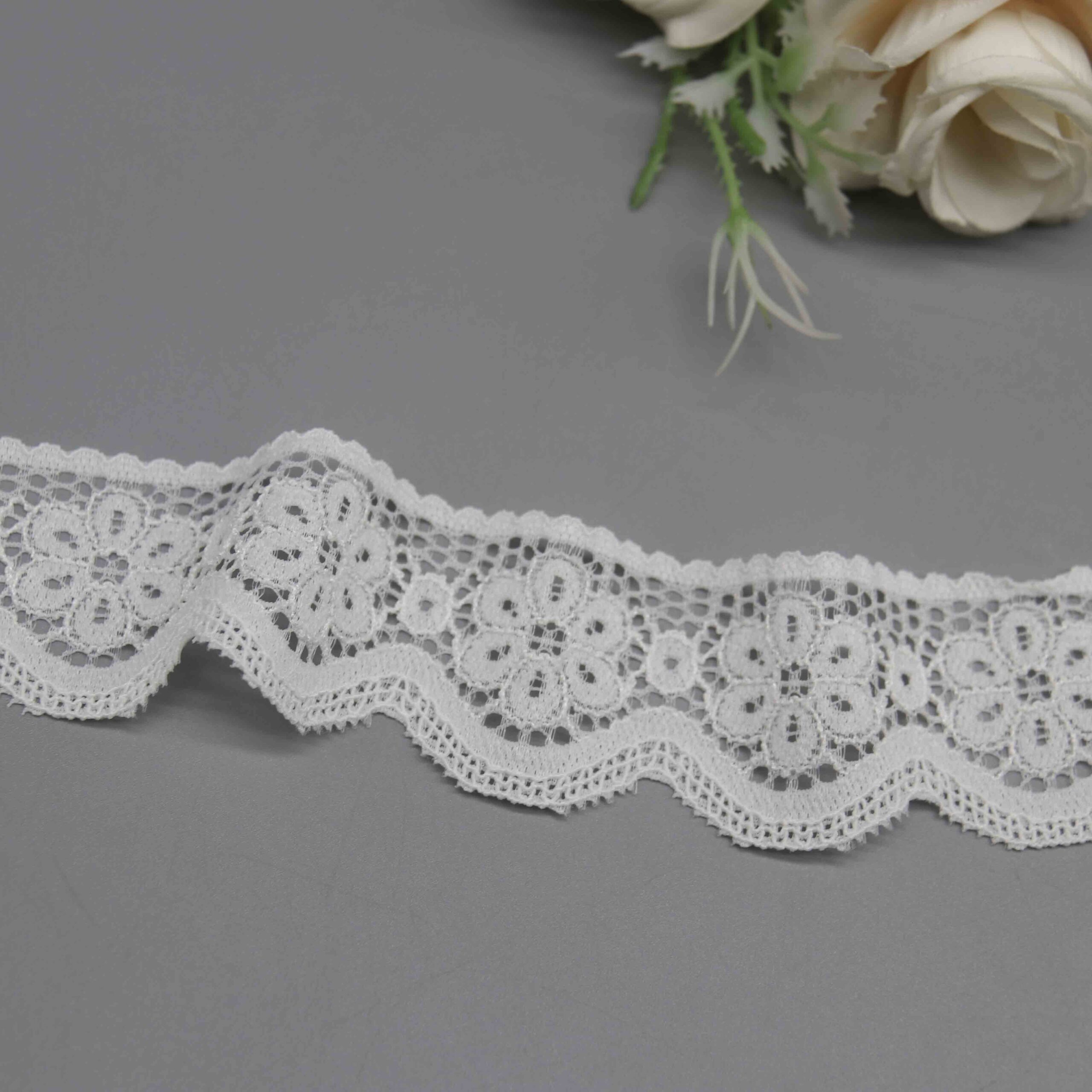 A studio photo of a 3.5cm white galloon lace trim featuring a pattern of connected floral medallions and a scalloped edge