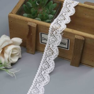 A close-up studio photograph of a 2.5cm wide white wavy stretch lace trim, showcasing its serpentine pattern and scalloped edges.