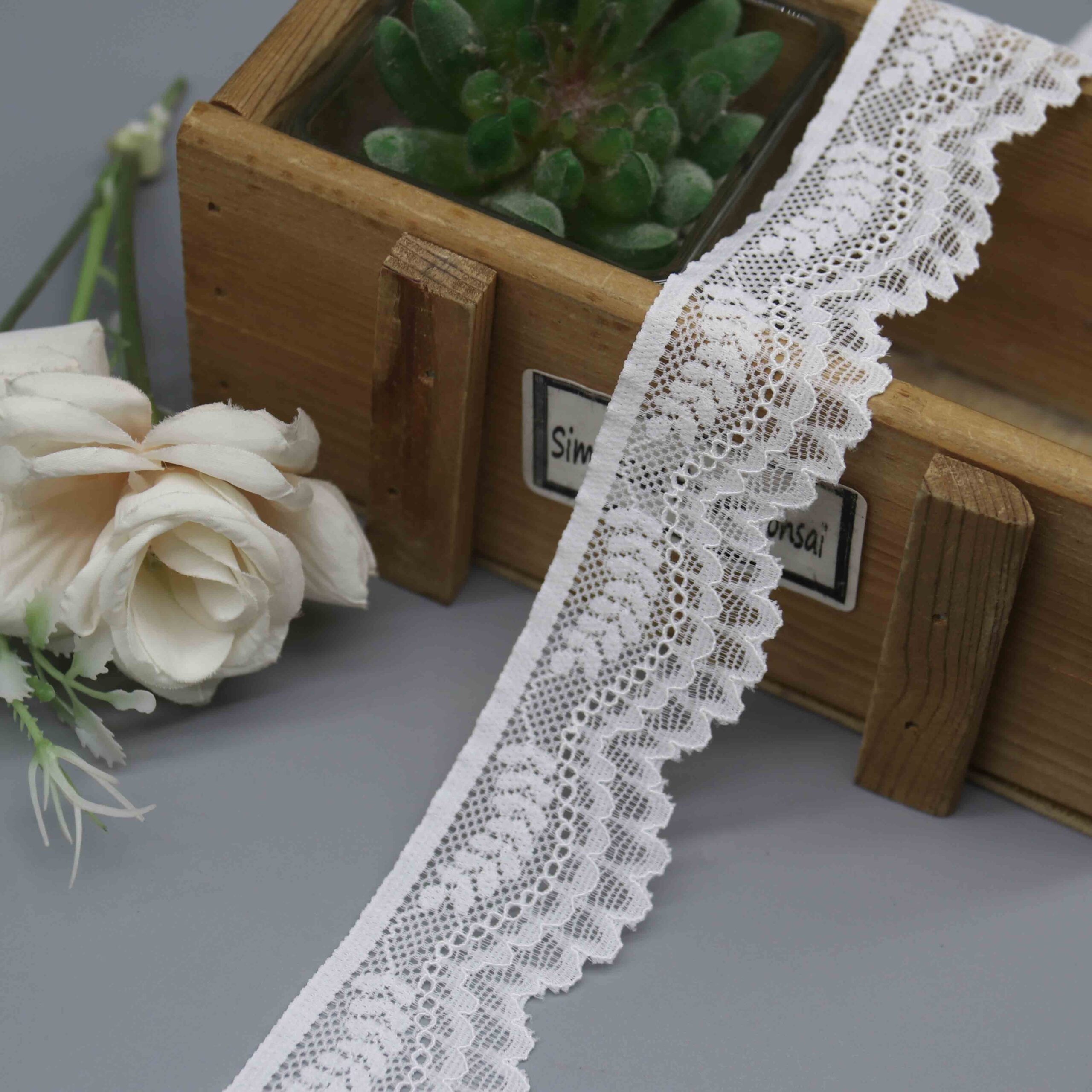 A studio product shot of a 3.3cm wide white floral stretch lace trim, showing its asymmetrical design with a straight sewing edge