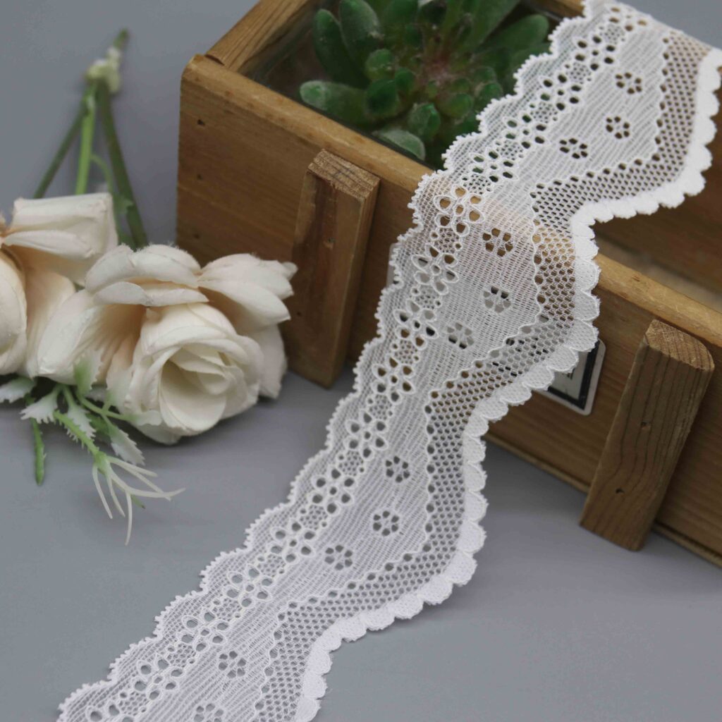 Studio product photo of a 4.5cm wide white stretch lace trim with symmetrical scalloped edges and a floral eyelet pattern.