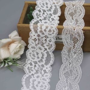 Two widths of a white floral stretch lace trim with scalloped edges, displayed in a wooden box with a decorative flower