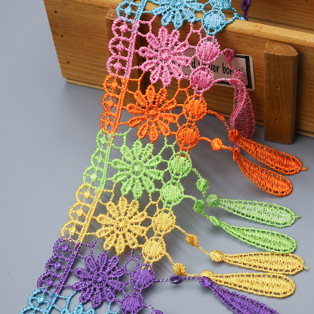 Multicolor water soluble lace trims featuring intricate floral embroidery and tassel accents displayed on a wooden box.