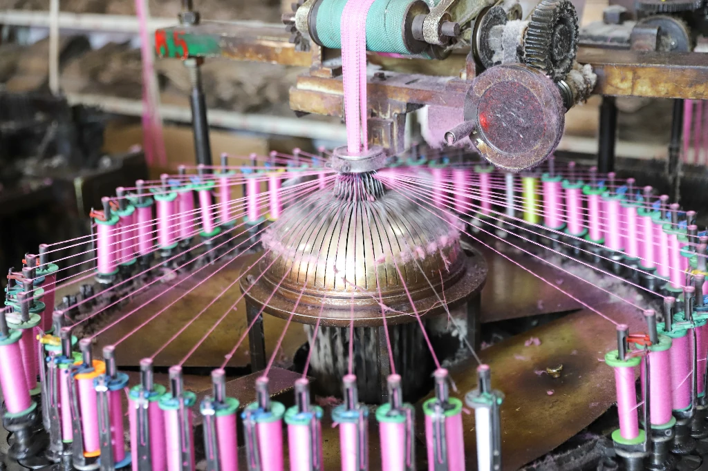 Employee threading yarn into industrial lace-making equipment.