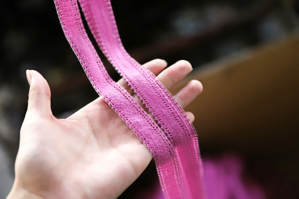 Hand holding vivid pink water soluble lace, showing flexibility and fine texture.