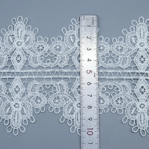 Elegant white French lace in wide design, 100% polyester and water soluble, ideal for garment trims.