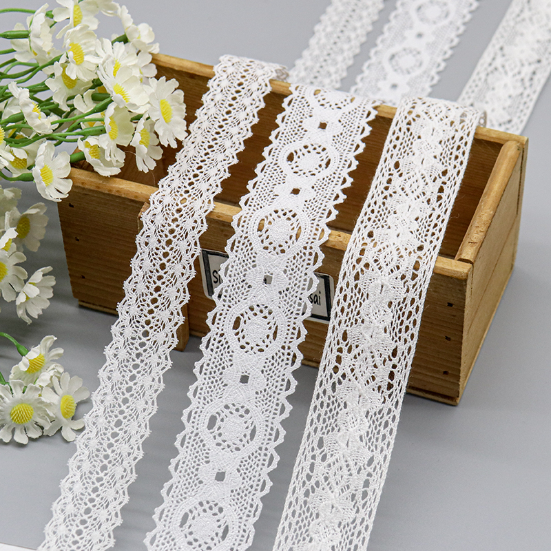 White cotton thread lace trims featuring detailed crochet designs displayed on a wooden box next to white daisies.