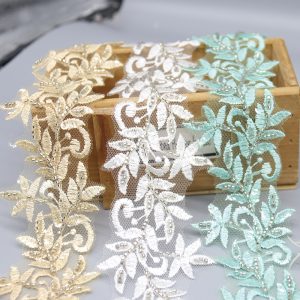 Close-up of gold leaf embroidered lace trim with bead accents, crafted on transparent mesh fabric.