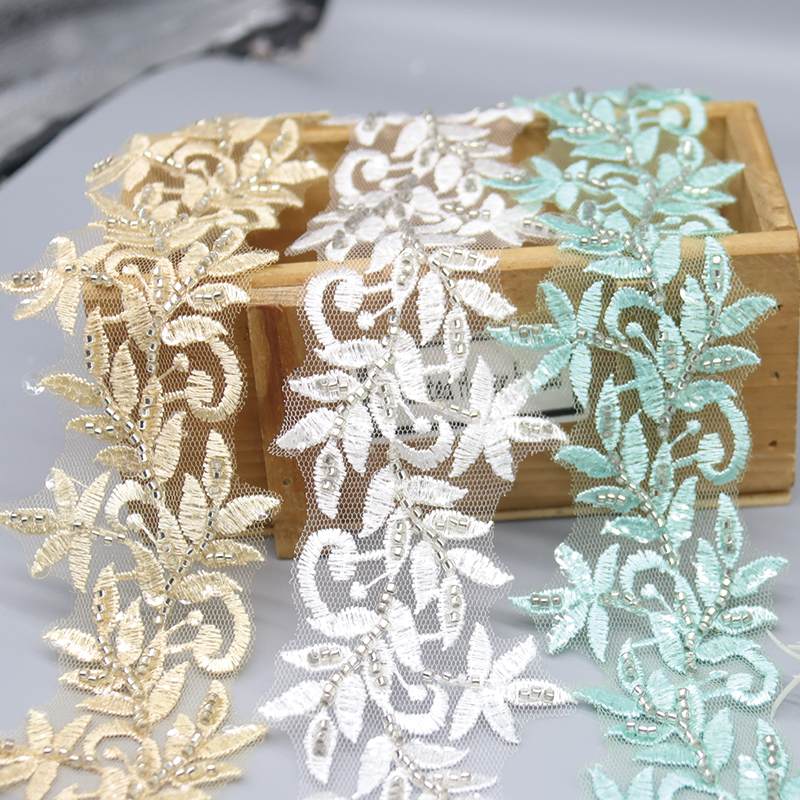 Close-up of gold leaf embroidered lace trim with bead accents, crafted on transparent mesh fabric.