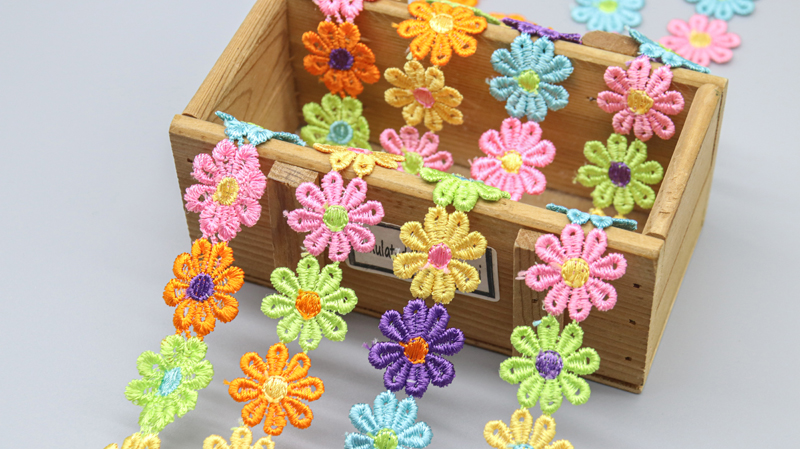 Bright and cheerful water soluble floral lace featuring a variety of daisy colors, suitable for apparel edging and fun home décor ideas.