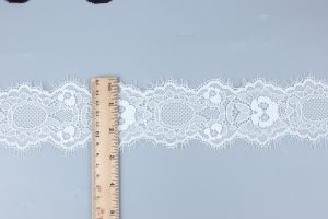Pure white crocheted lace with intricate beaded flower motifs paired with timeless embroidered lace trim, crafted for couture garment details.