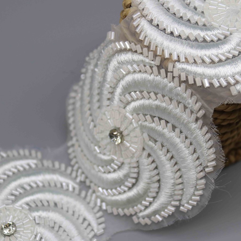 Close view of narrow embroidered lace for collars and cuffs contrasted with structured single face grosgrain ribbon suited to waistlines for accelerated production.