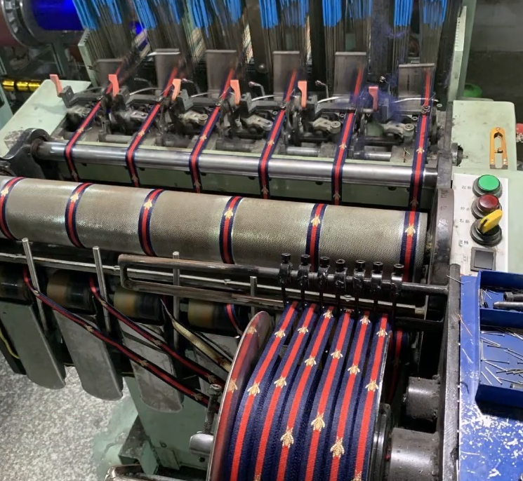 Close-up of quality-control stations and computerized machines for piping cord insertion and grosgrain weaving, demonstrating sample runs and testing for durable, soft lace trims for apparel OEMs.