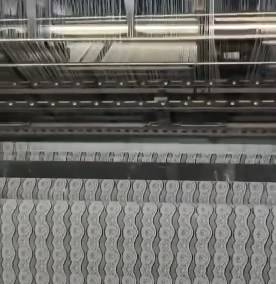 Row of multi‑needle computerized embroidery machines producing delicate lace trims for apparel, lingerie, and home textiles inside a modern factory.