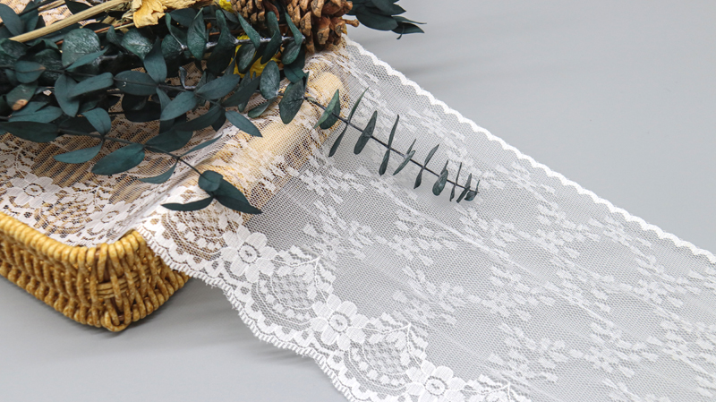 Close-up display of intricately detailed white floral embroidered lace trim beside shimmering luxury lace trim, highlighting popular choices for OEM dress production.