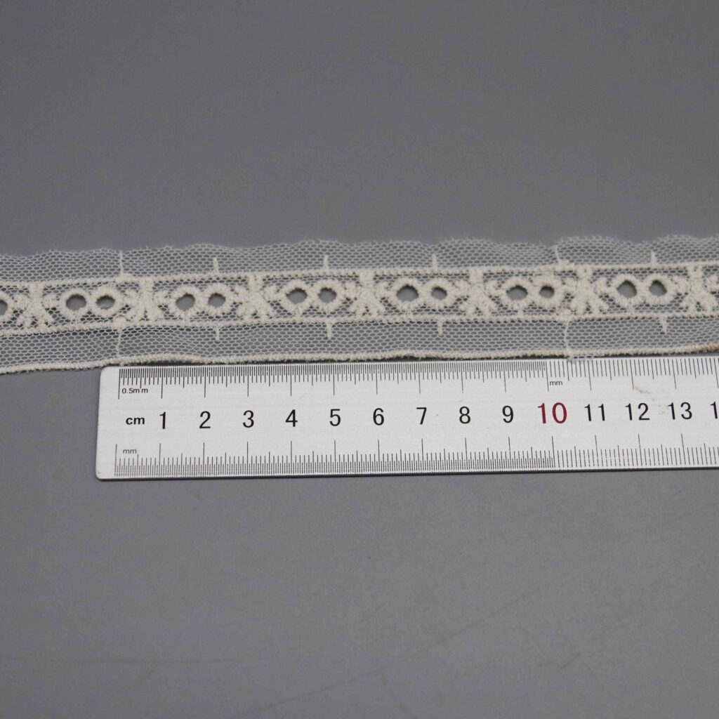 Ruler laid horizontally along the butterfly eyelet pattern repeat showing scale and motif spacing