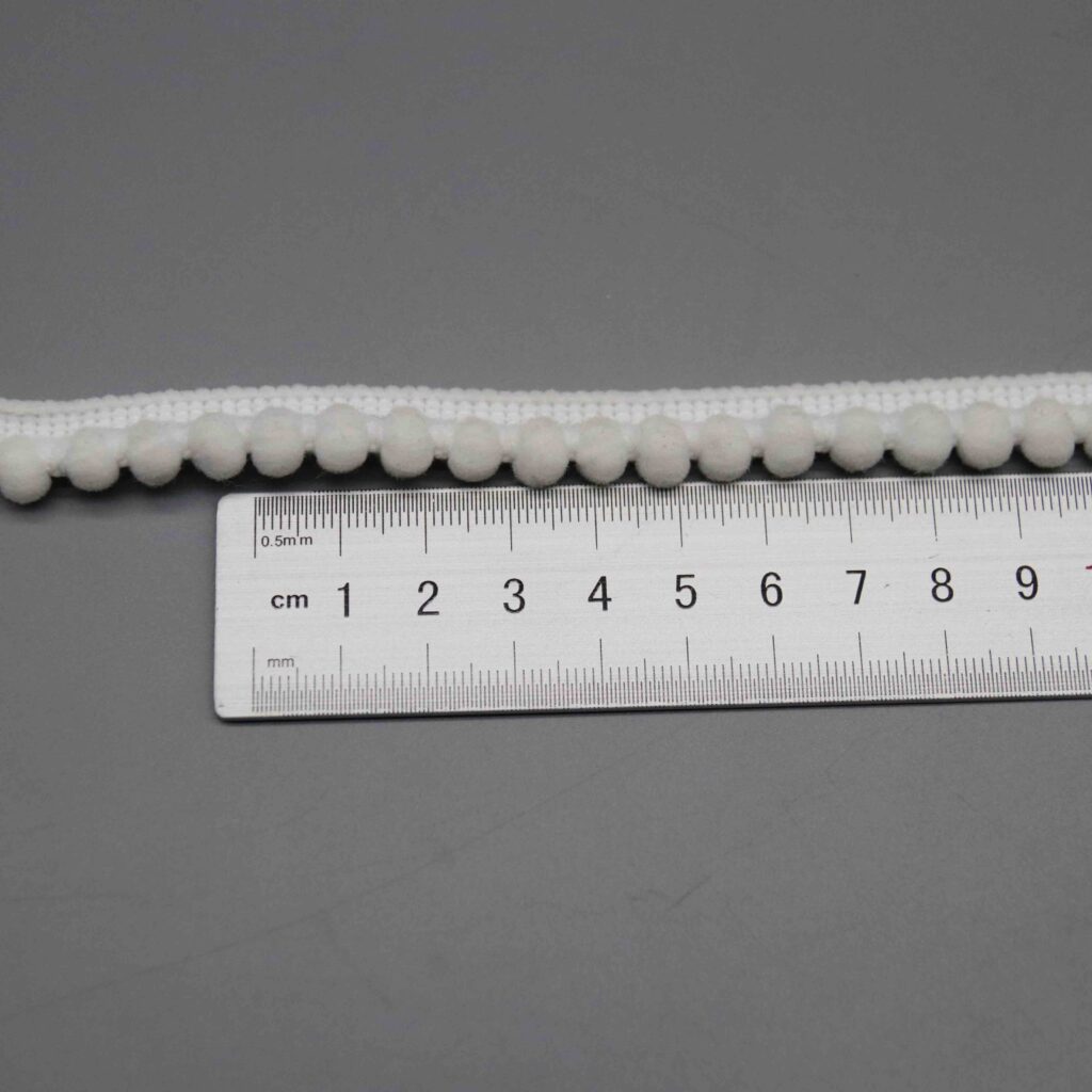 Ruler laid vertically across the pompom trim showing the exact 1cm width measurement