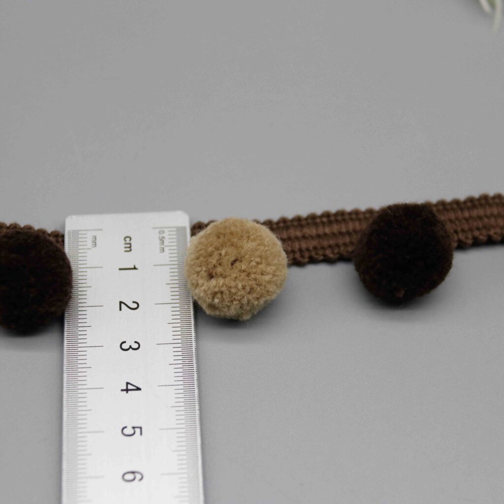Ruler laid vertically across the pompom trim showing the exact 2.5cm width measurement